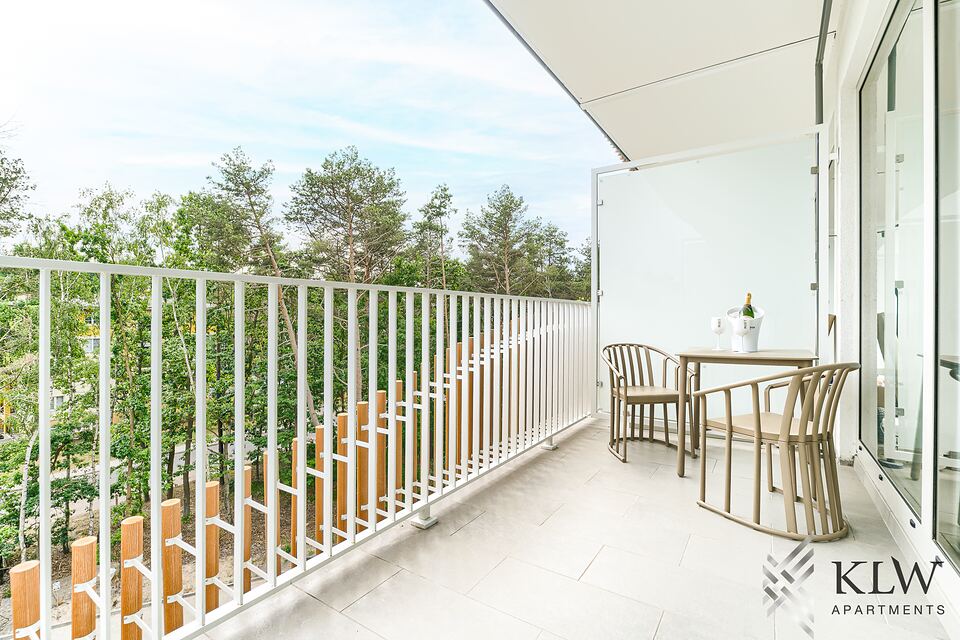Balkon apartamentu ze stolikiem i krzesłami, za balustradą sosny